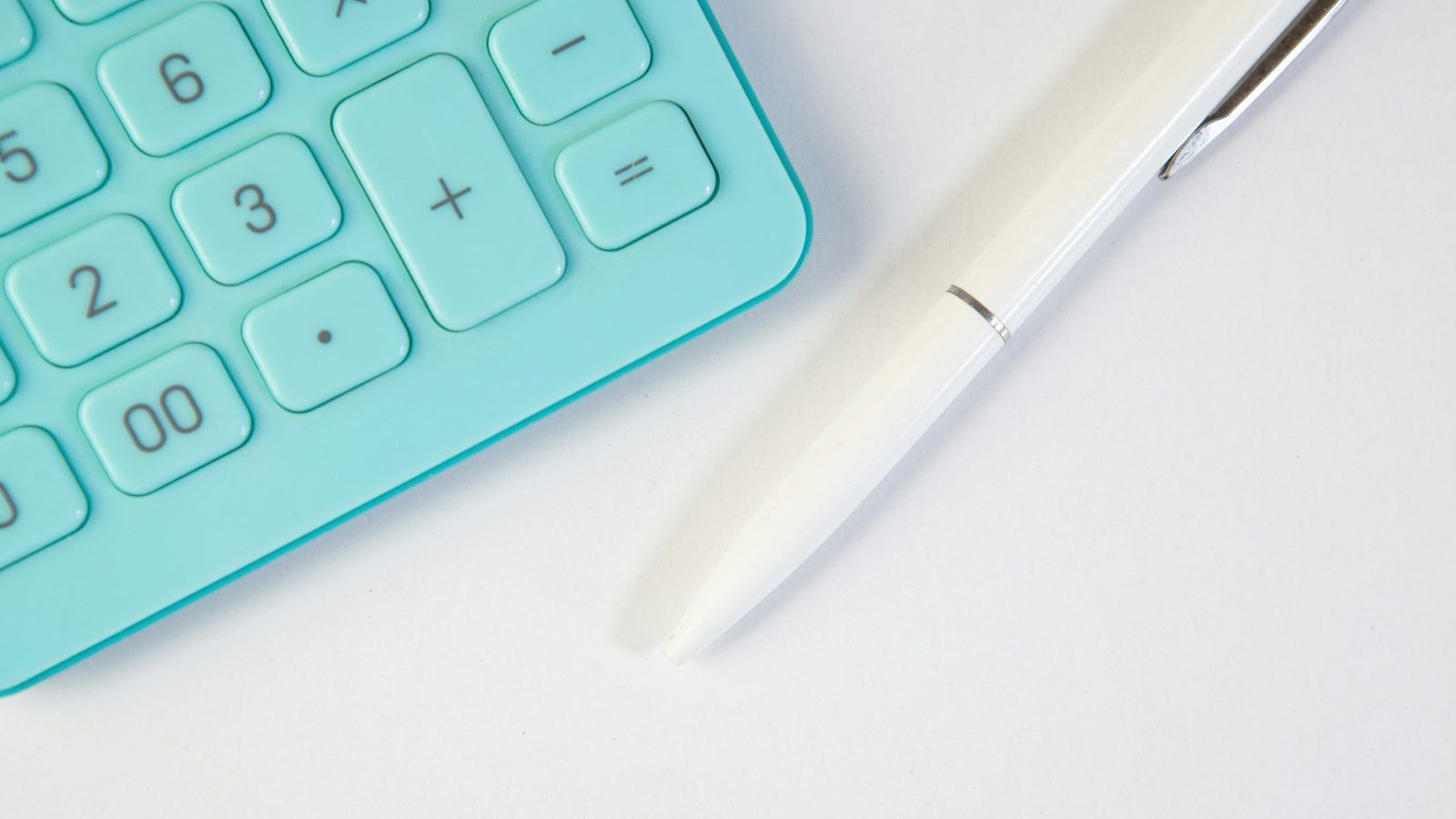 Close-up of a turquoise calculator keypad and a white pen on a plain white desk