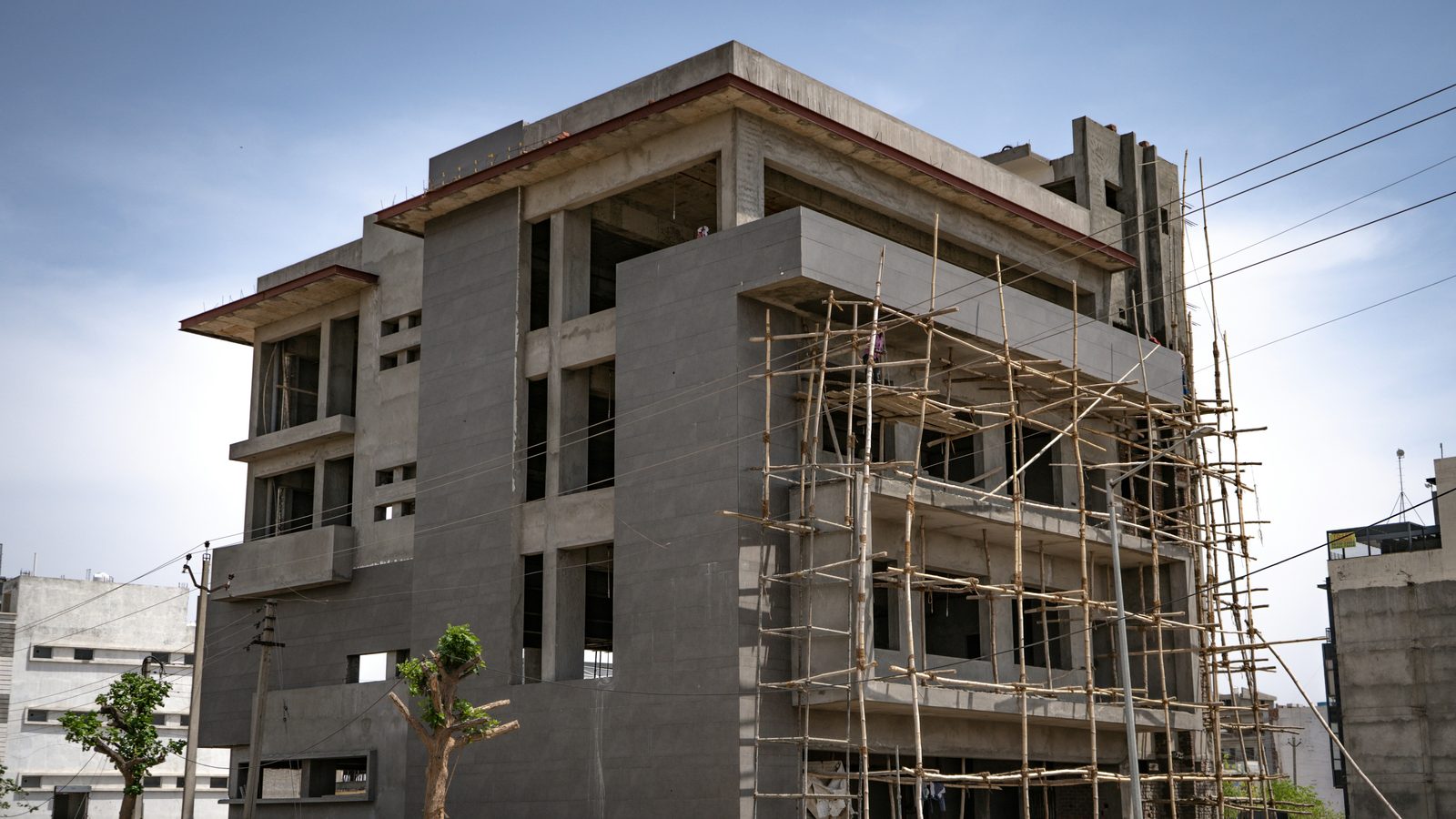 A part-built concrete building wrapped in bamboo scaffolding, seen from street level against an open sky