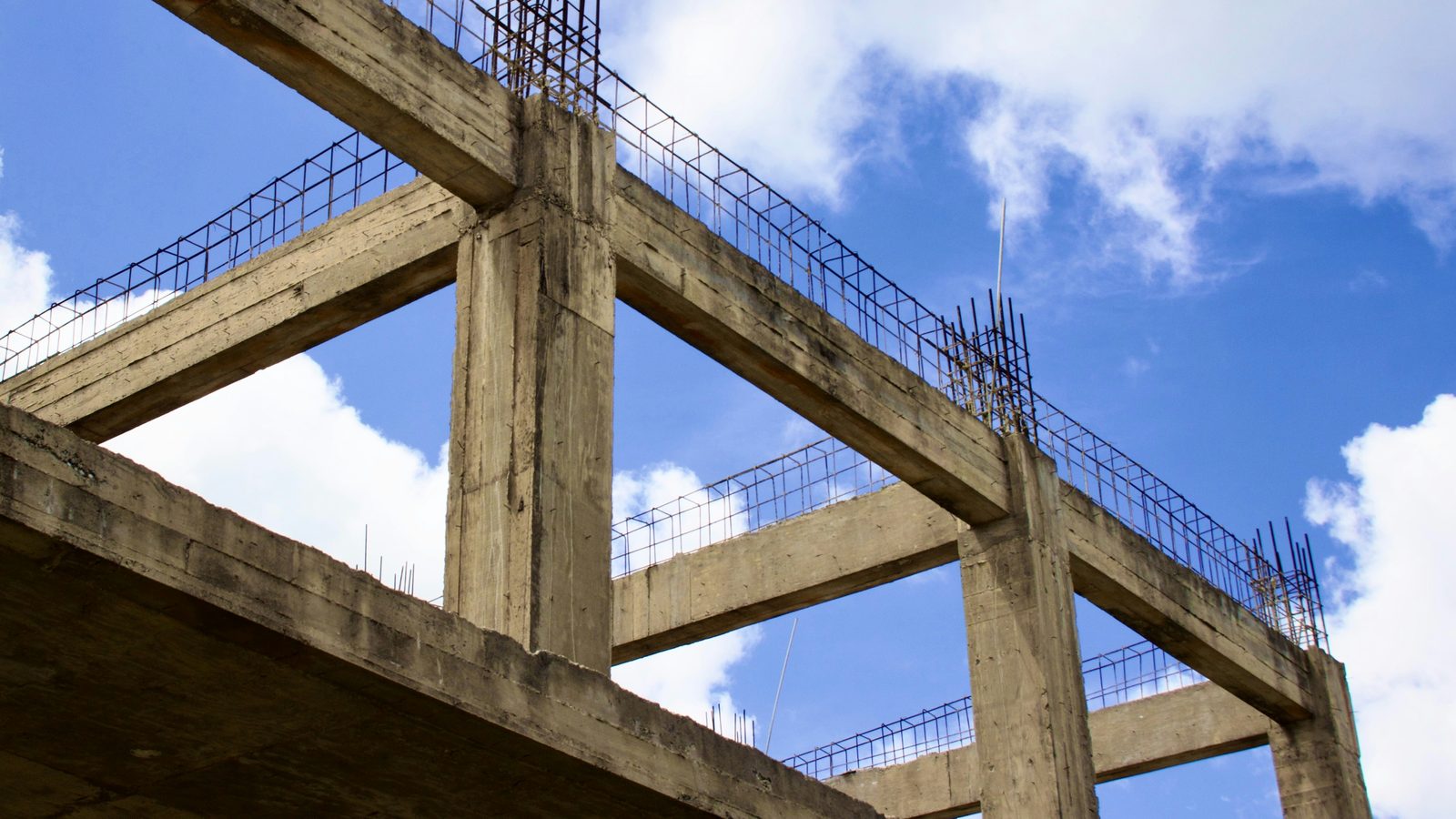 Concrete columns and beams with exposed steel reinforcement, against the sky